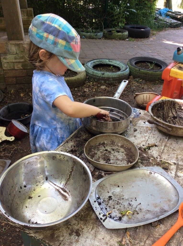 A little girl is playing in the mud with pots and pans.