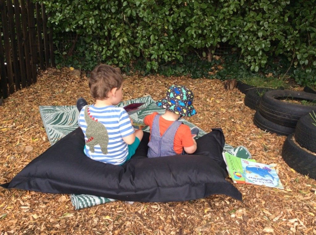 Two young boys are sitting on a bean bag chair in the dirt.