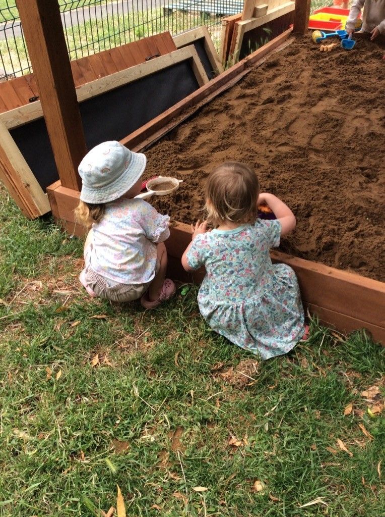 Two little girls are playing in a sandbox.