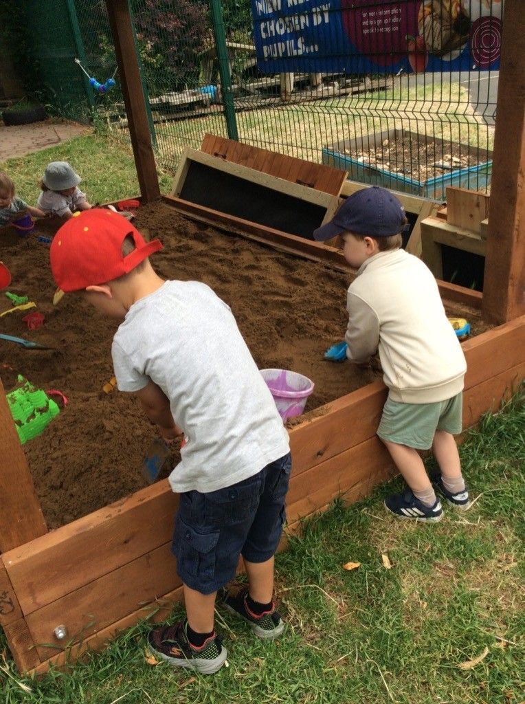 Two young boys are playing in a sandbox.