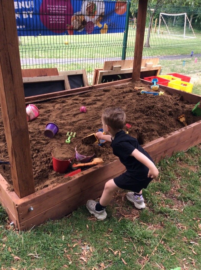 A young boy is playing in a sandbox with toys.