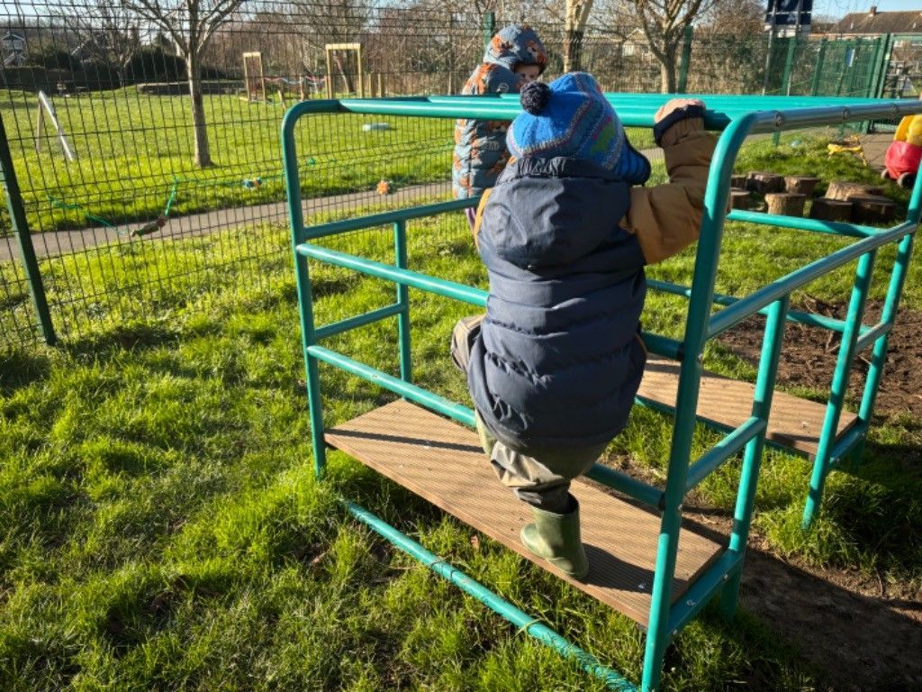 A child is climbing on a green metal structure in a park.