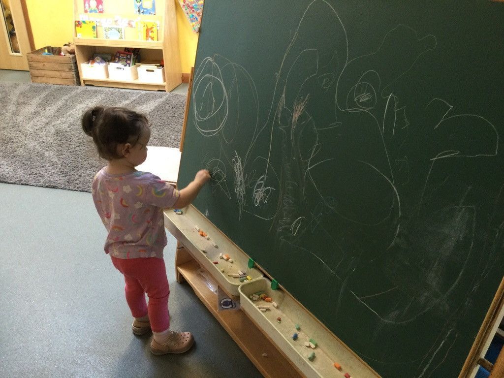 A little girl is drawing on a blackboard with chalk.