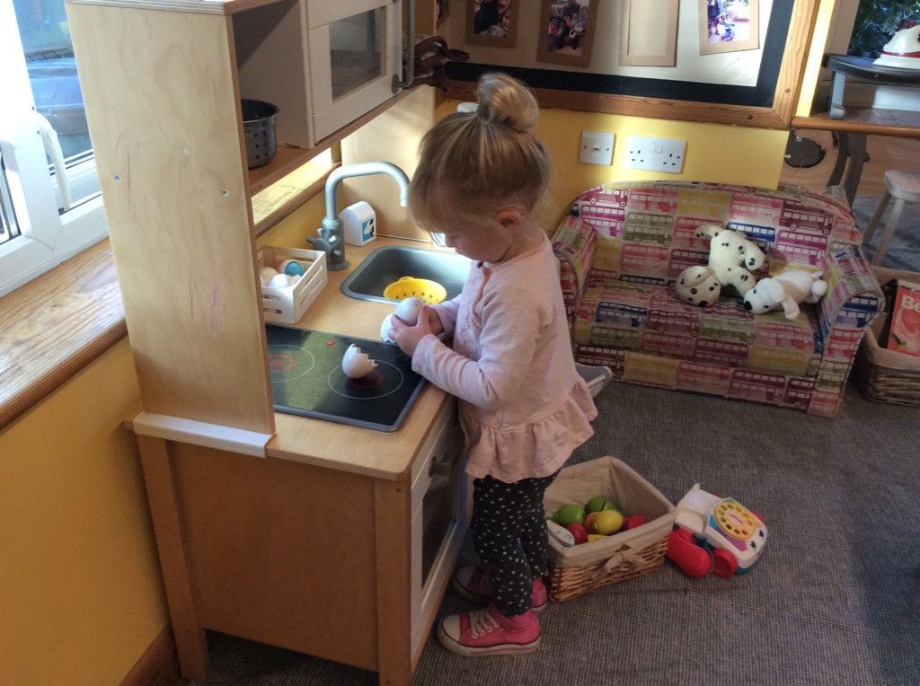 A little girl is playing in a wooden play kitchen.