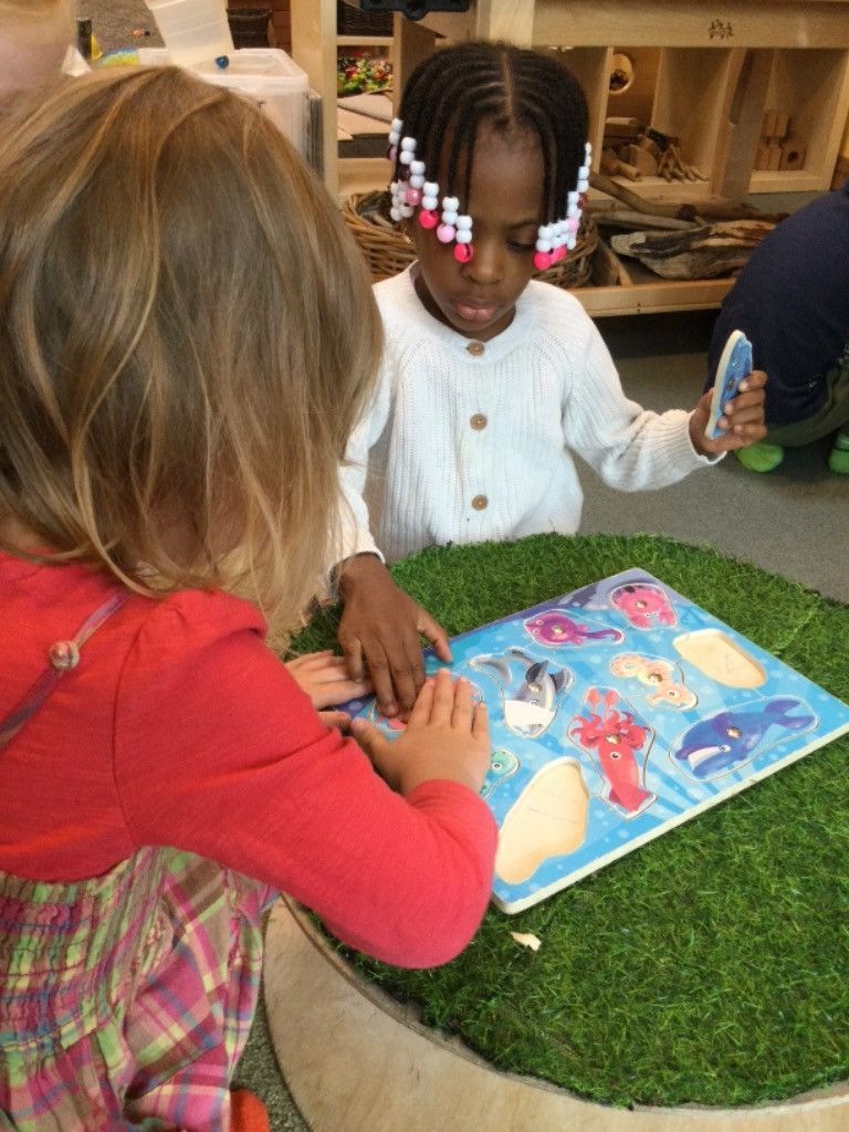 Two young girls are sitting at a table playing with a book.