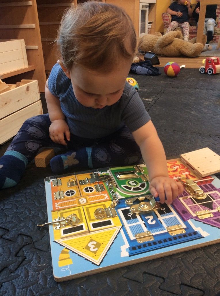 A baby is playing with a wooden puzzle on the floor.