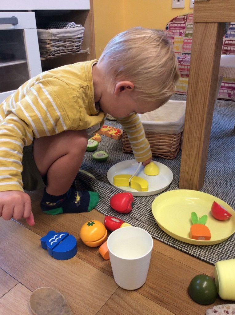 A young boy is playing with wooden fruits and vegetables on the floor.