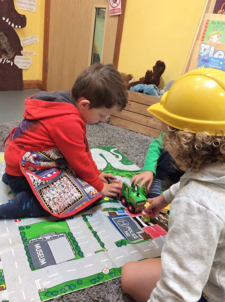 Two young boys wearing hard hats are playing with toy cars on the floor.