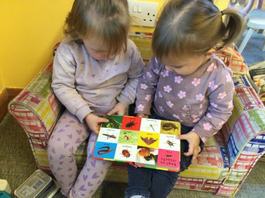 Two little girls are sitting on a chair reading a book