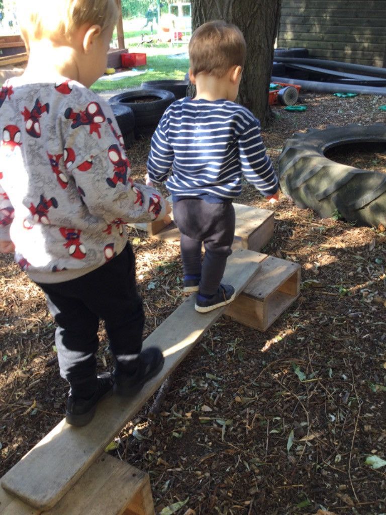 Two young boys are standing on a wooden balance beam.