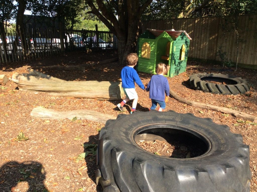 Two children are standing next to a large tire in a playground.