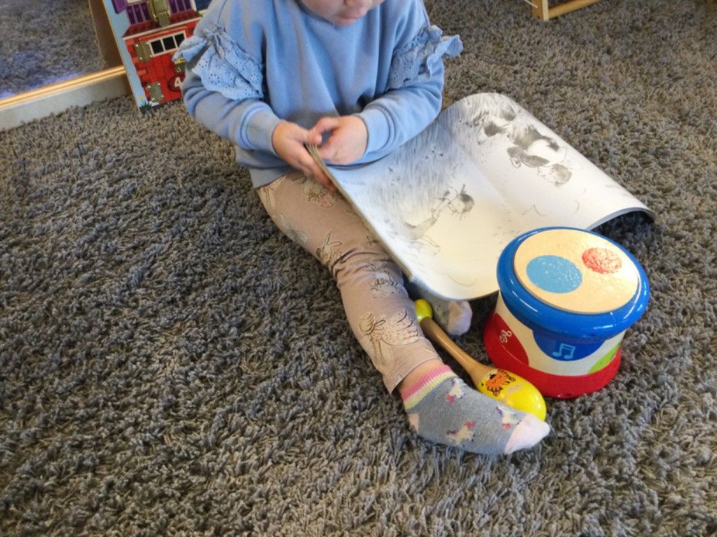 A little girl is sitting on the floor with a drum and a book.