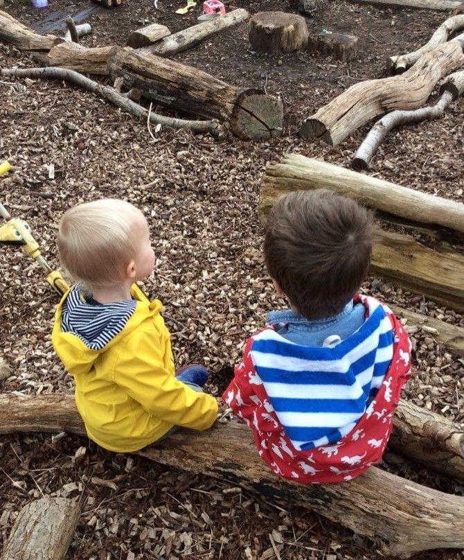 Two young boys are sitting on a log in the dirt.