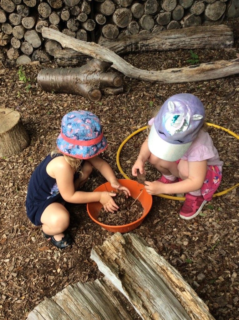 Two little girls are playing with a bowl of dirt on the ground.