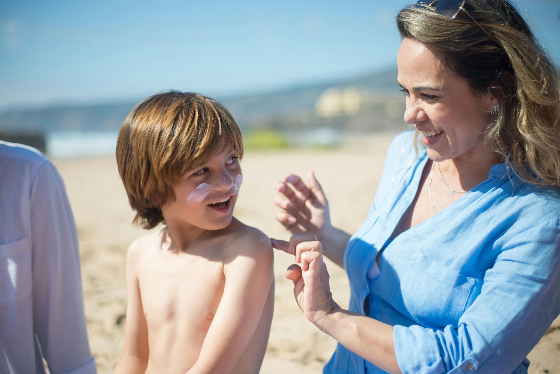 A woman is applying sunscreen to a young boy 's arm on the beach.
