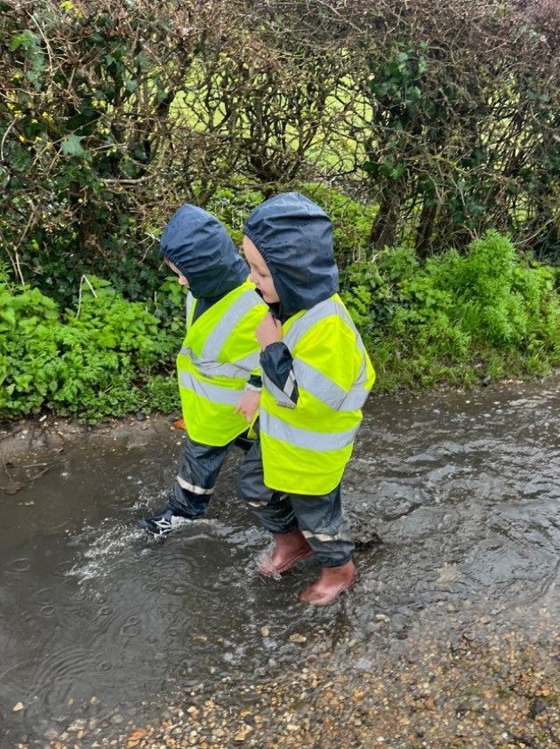 Two little boys are walking through a puddle of water.