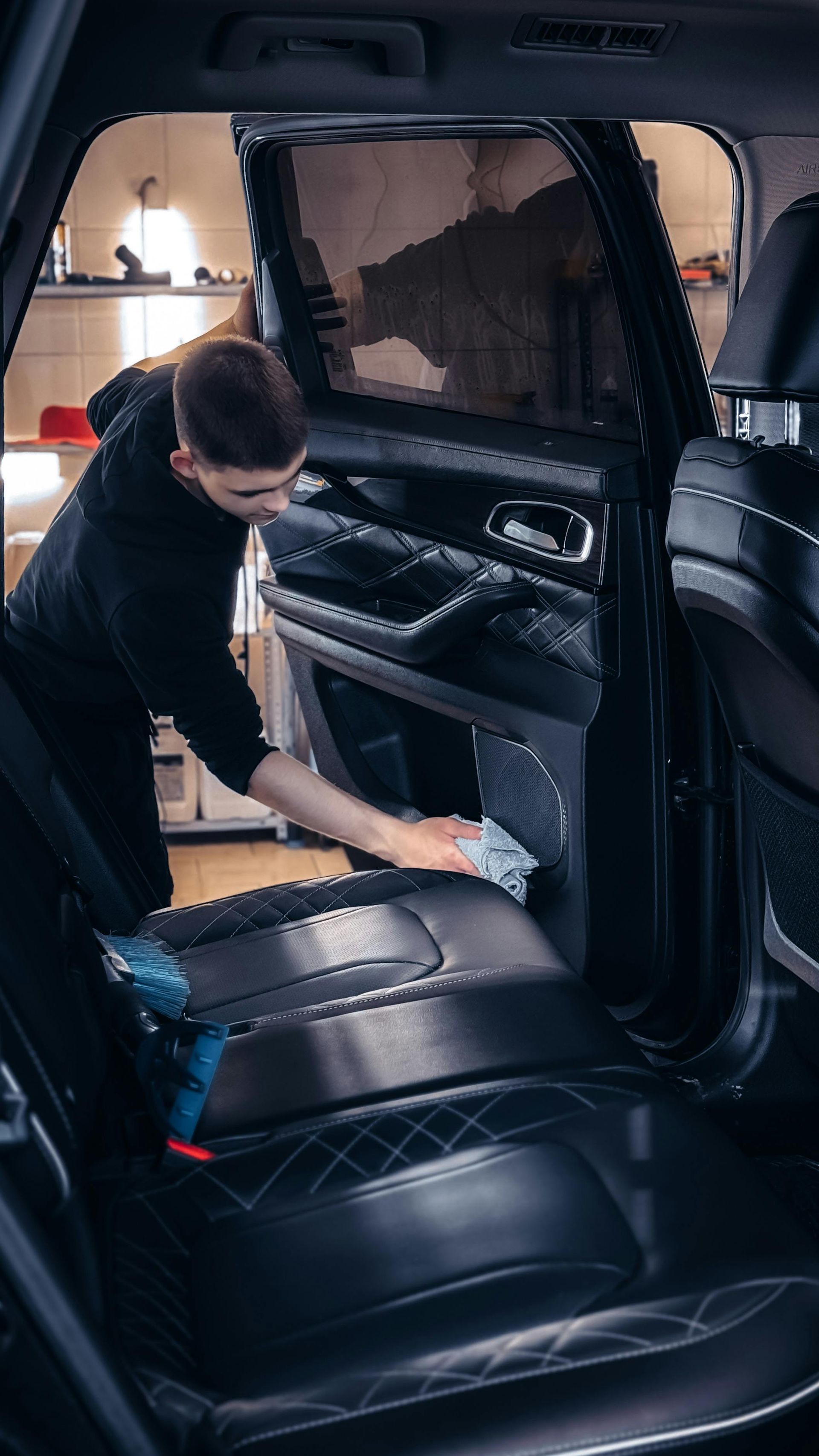Person cleaning the back seat of a black car interior with a cloth