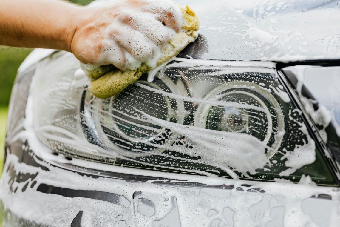 Hand washing a car window with soap suds and a yellow sponge