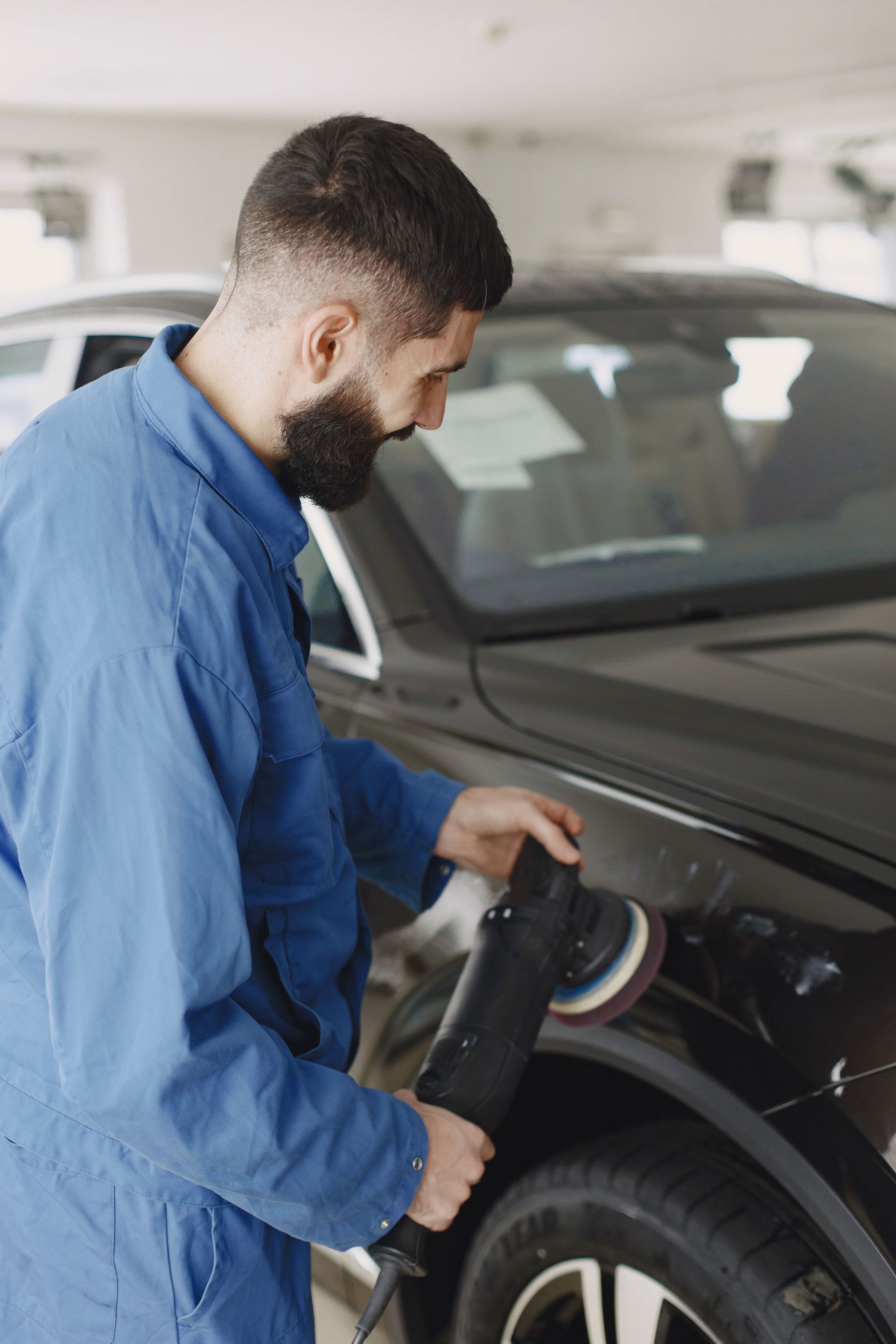 Man in blue shirt using a pressure washer to clean a black car in a garage