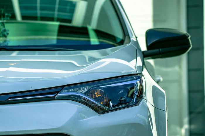 Close-up of a white car’s front headlight and side mirror in a showroom or parking area.