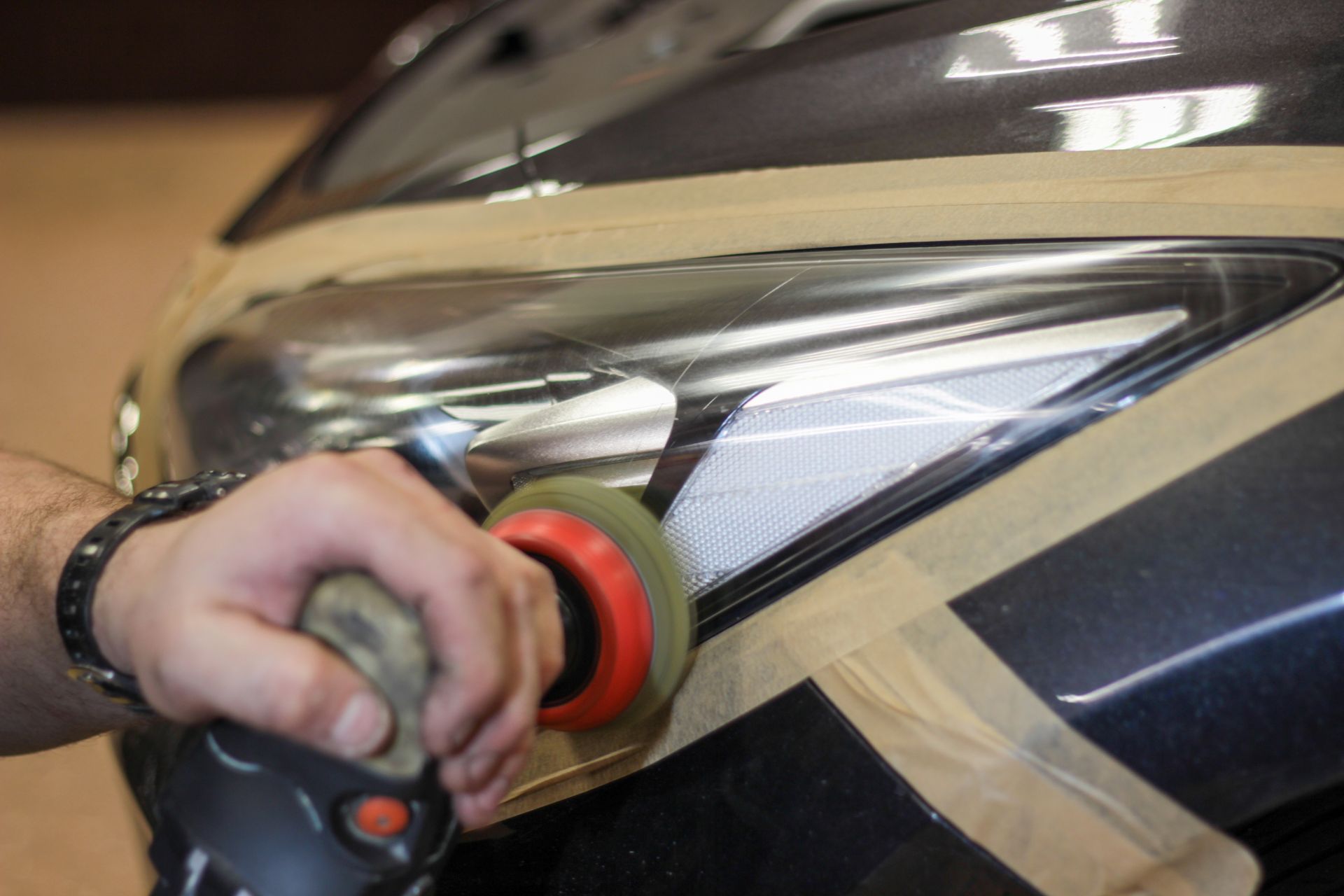 A hand polishes a car’s headlight with a buffer, reflecting light on the silver body.