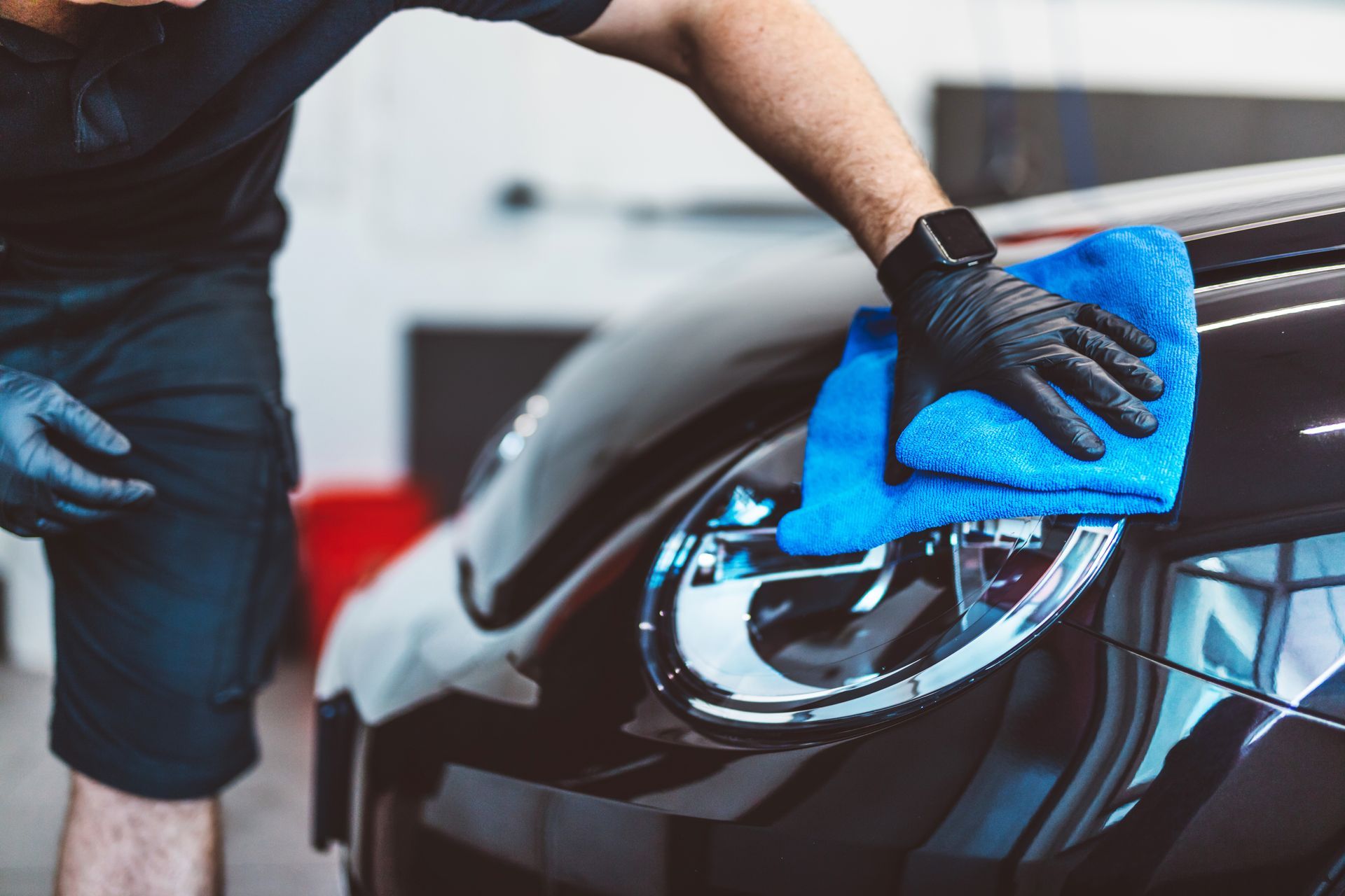 Person wiping a black car’s headlight with a blue cloth in a garage
