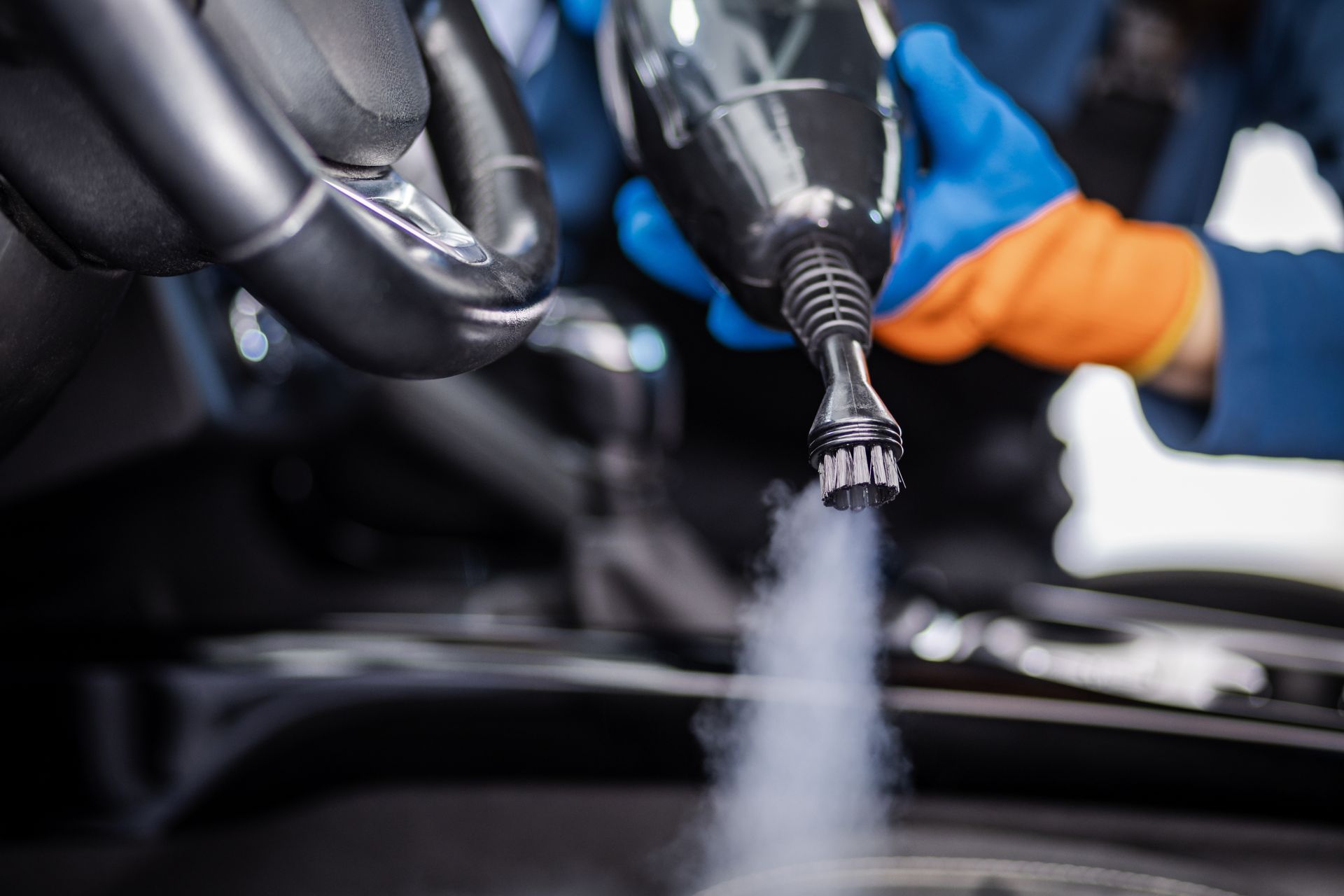Car wash nozzle spraying foam onto a car, with gloved hands in the background