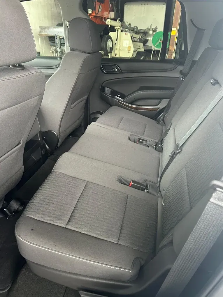 Car back seat with gray upholstery and folded center armrest, viewed from the rear door.
