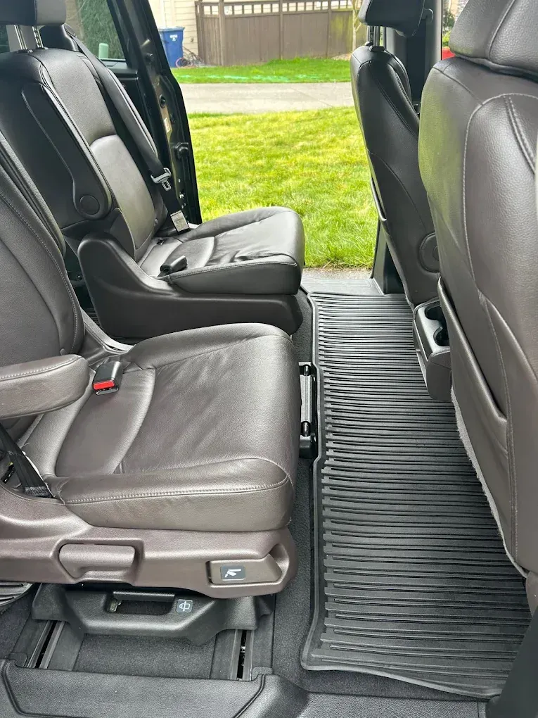 Car interior with fold-up seats and a ribbed floor mat, shown from the side door.