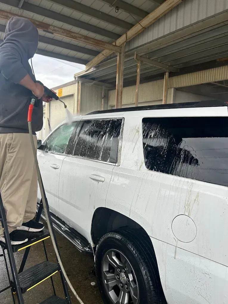 Person pressure-washing a white SUV under a carport