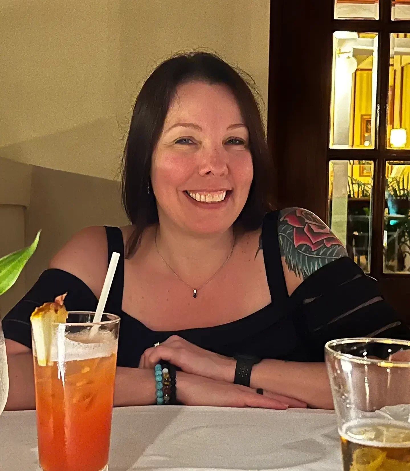 A woman sits at a table with a drink and a glass of beer