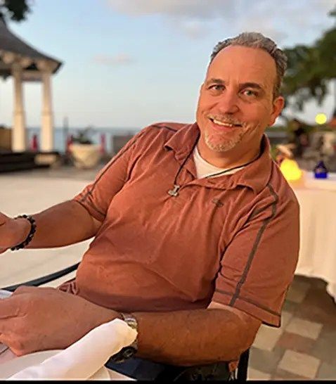 A man in a brown shirt is smiling while sitting at a table.