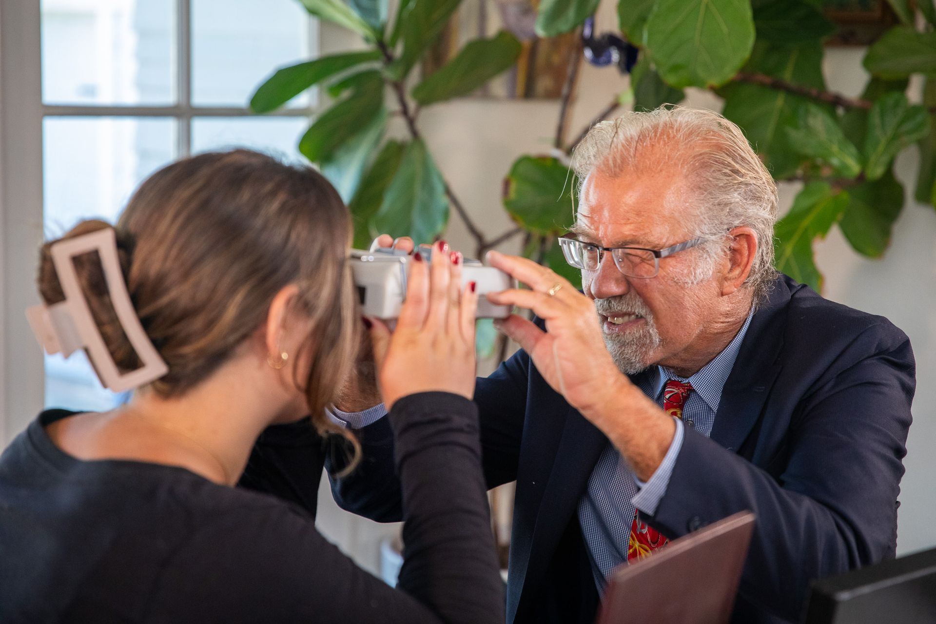 An eye care professional uses a handheld instrument to examine a patient's vision in a well-lit office.