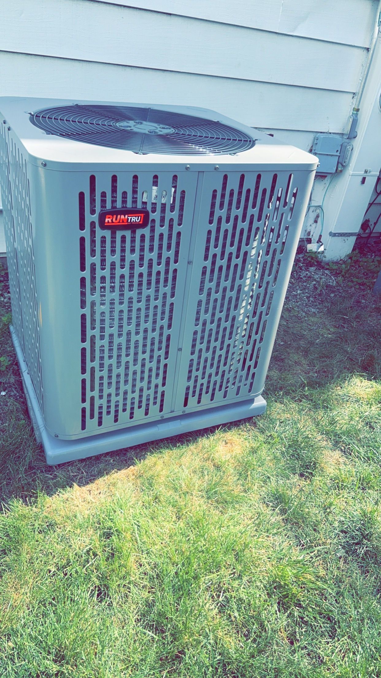 A large air conditioner is sitting in the grass next to a house.