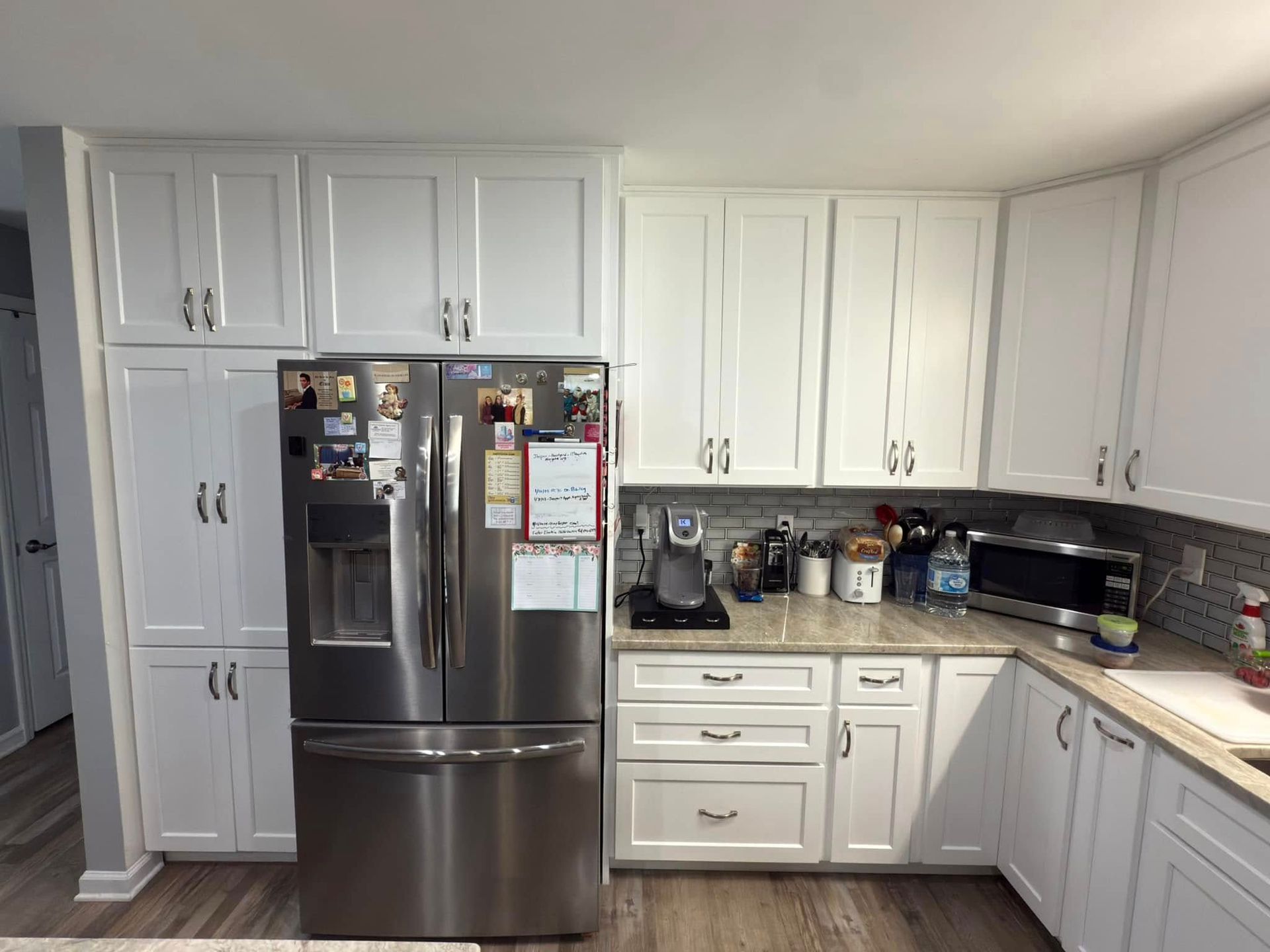 A kitchen with white cabinets and a stainless steel refrigerator.