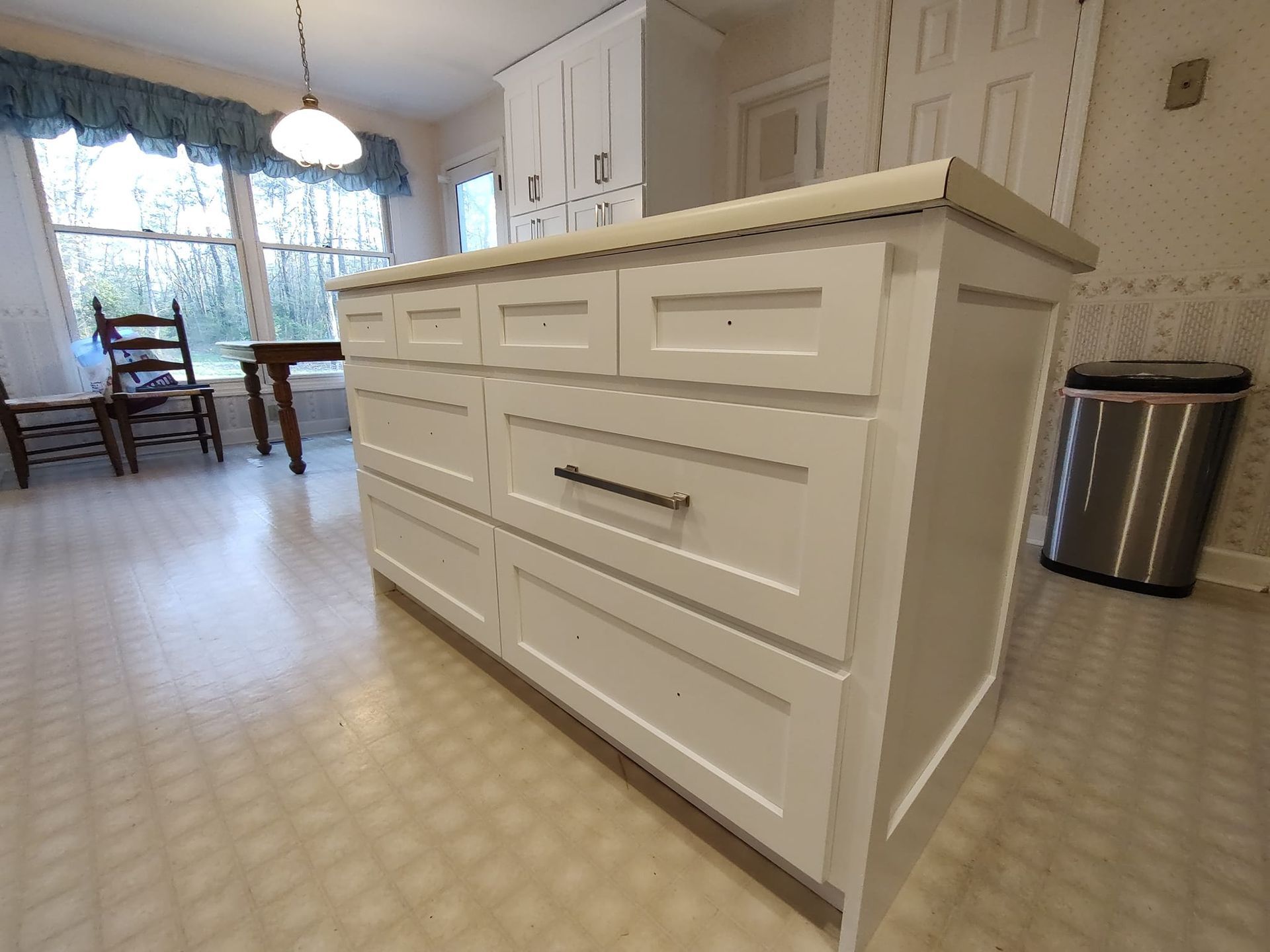 A kitchen with white cabinets and a stainless steel trash can