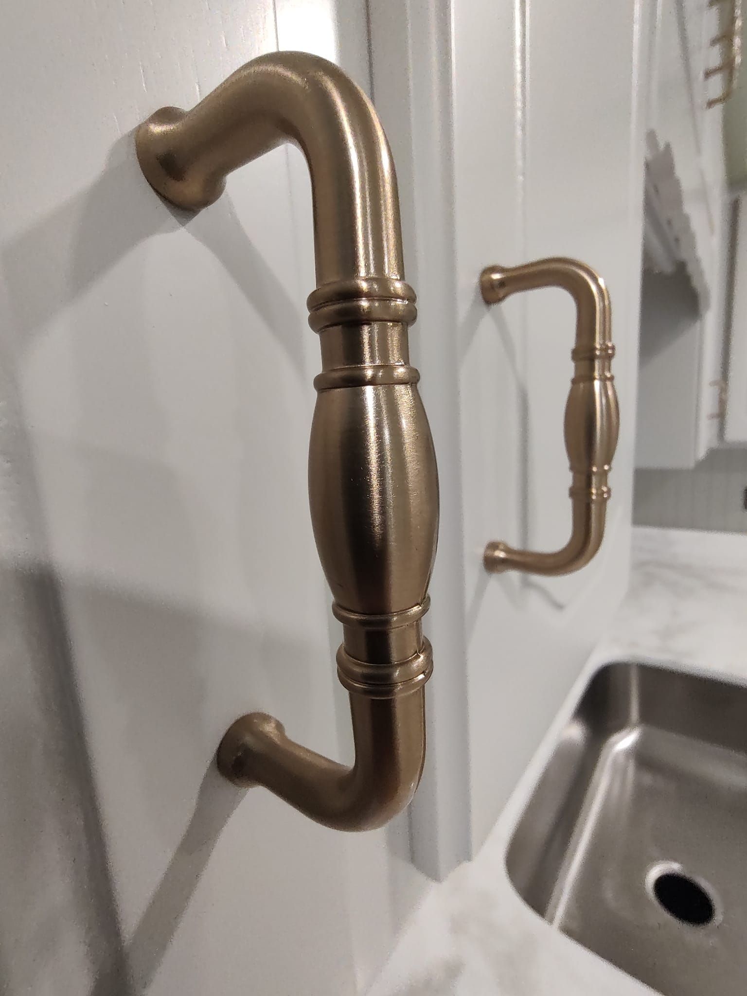 Two brass handles are hanging on a white cabinet next to a sink.