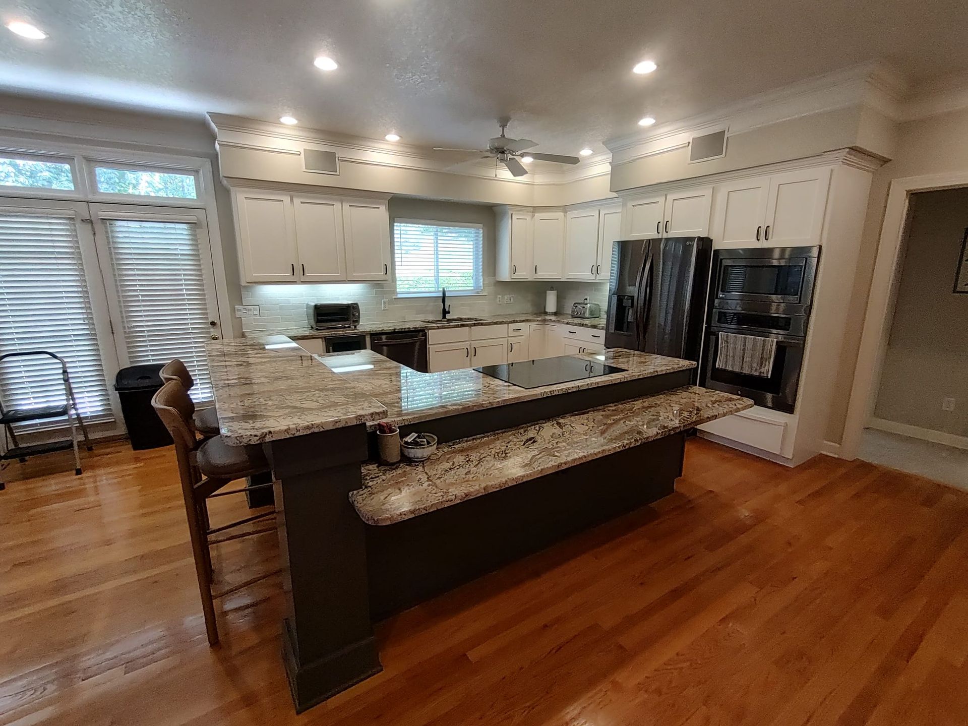 A kitchen with white cabinets , granite counter tops , stainless steel appliances and hardwood floors.