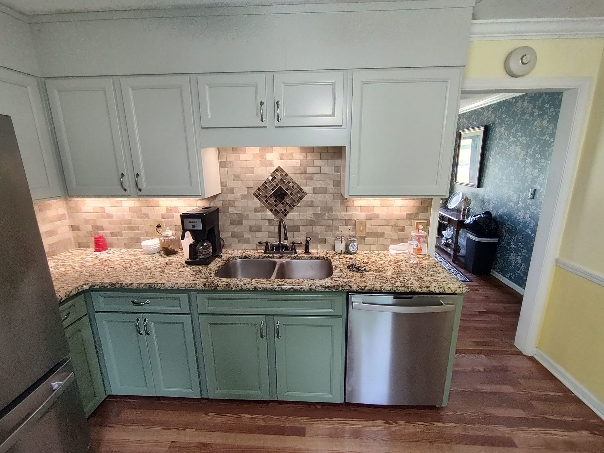 A kitchen with green cabinets , a sink , a refrigerator , and a dishwasher.