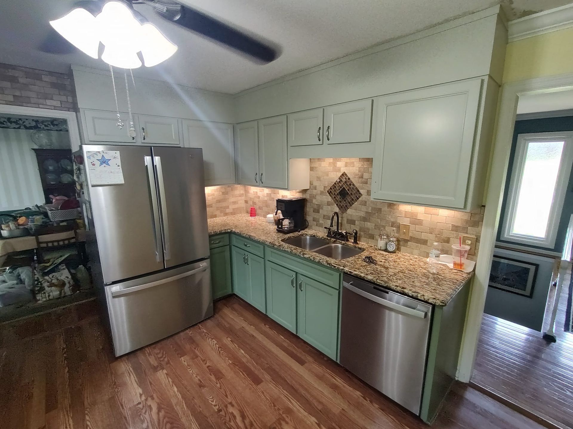 A kitchen with green cabinets , stainless steel appliances , a refrigerator and a sink.