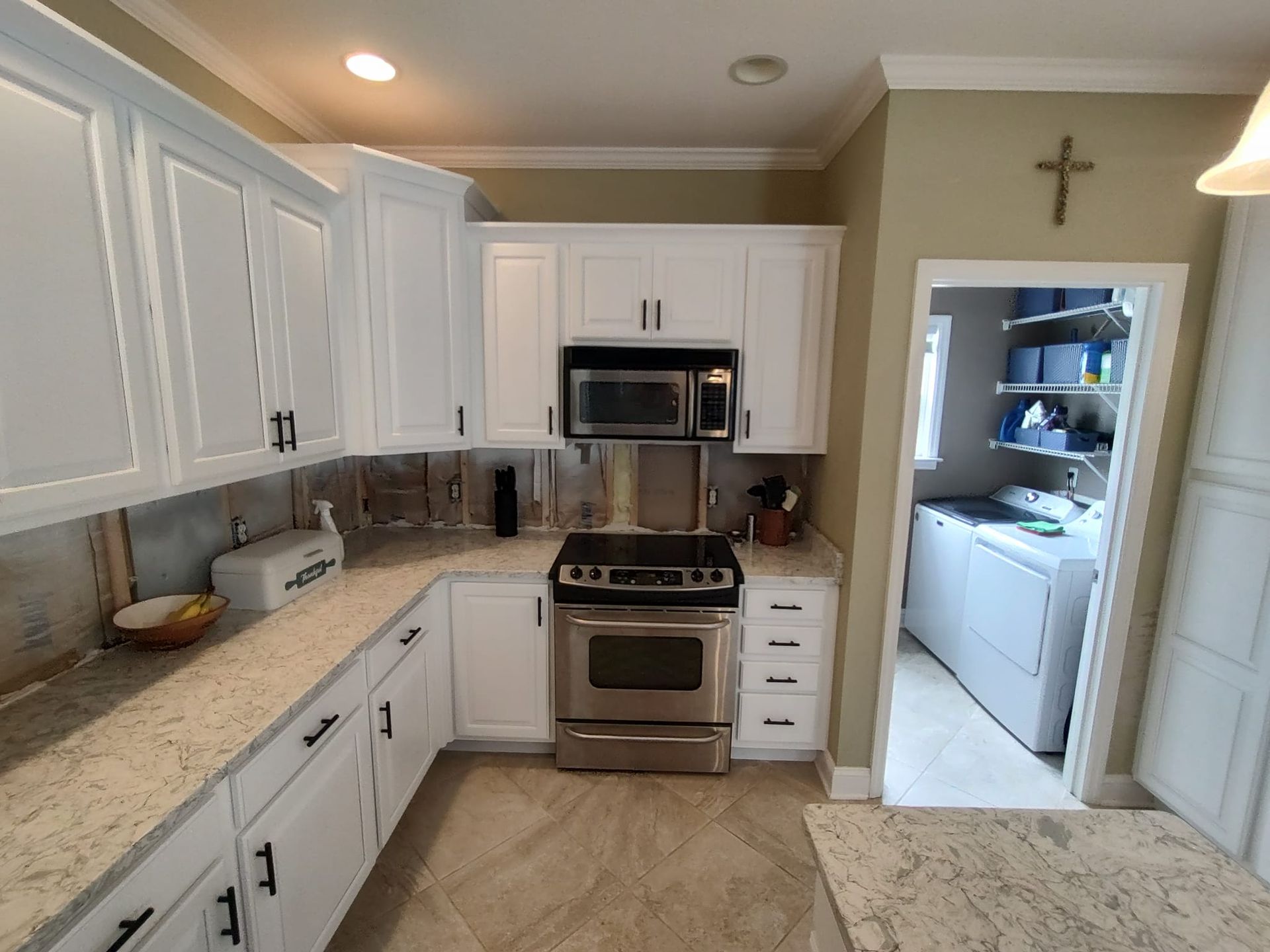 A kitchen with white cabinets and stainless steel appliances and a cross on the wall.