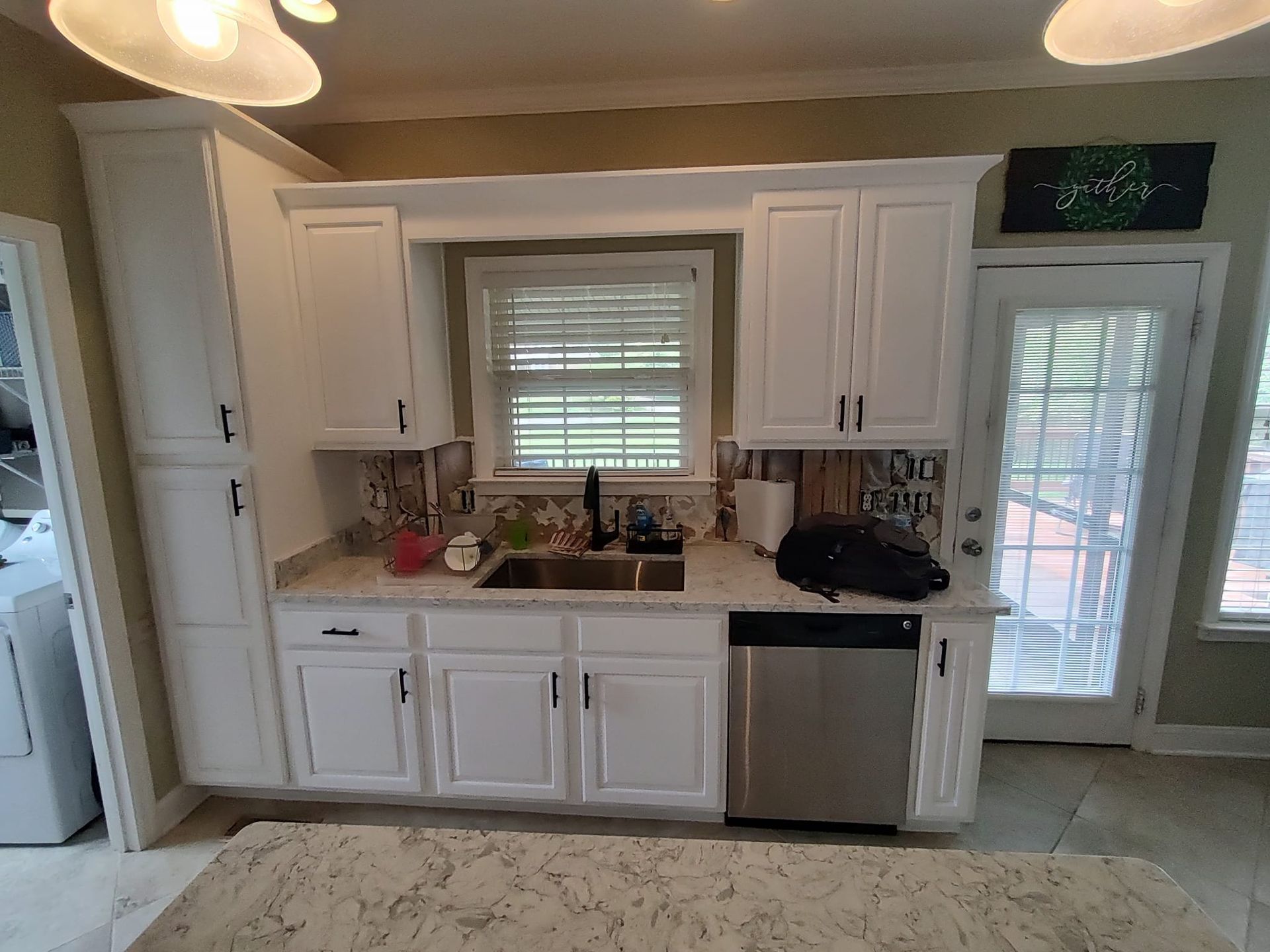 A kitchen with white cabinets , a sink , and a stainless steel dishwasher.