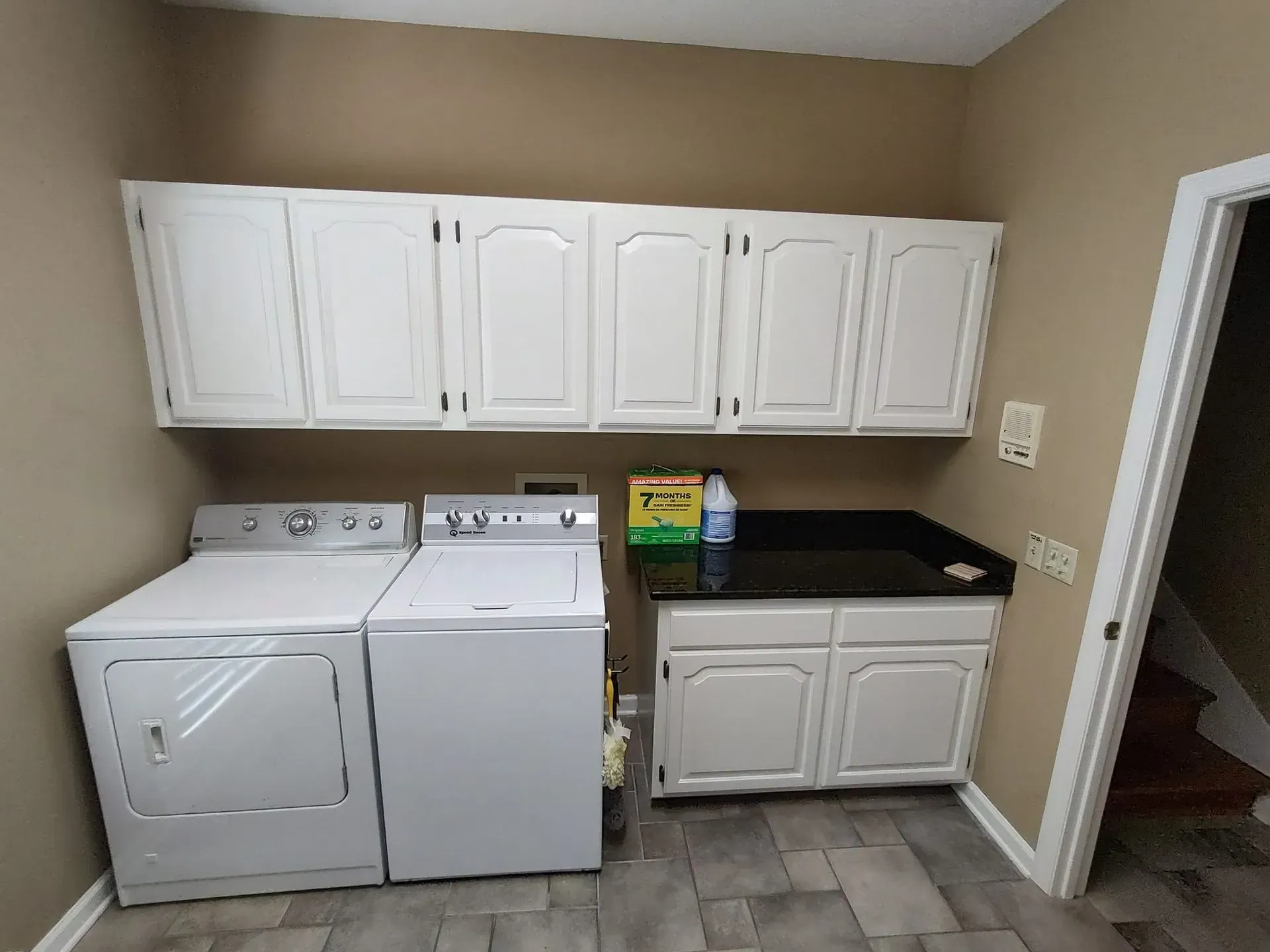 Laundry room with white appliances, cabinets, and a dark countertop.