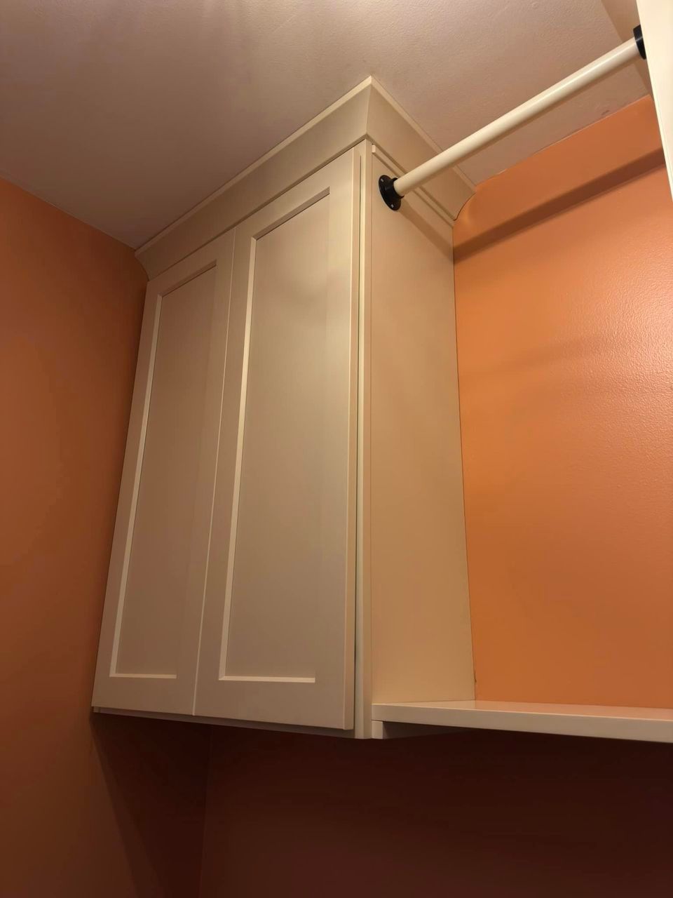 A laundry room with orange walls and white cabinets