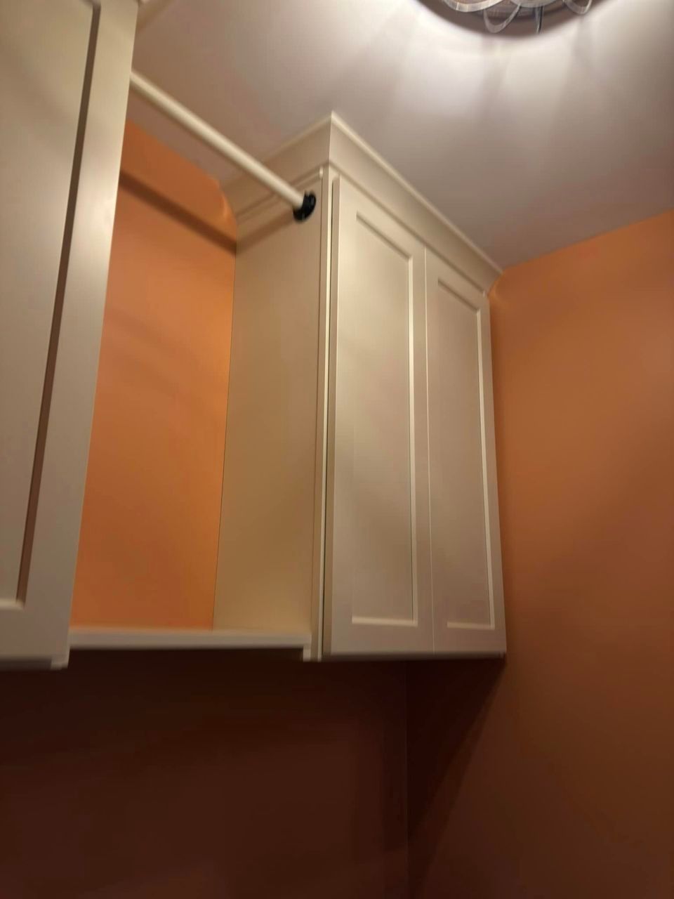 A laundry room with orange walls and white cabinets