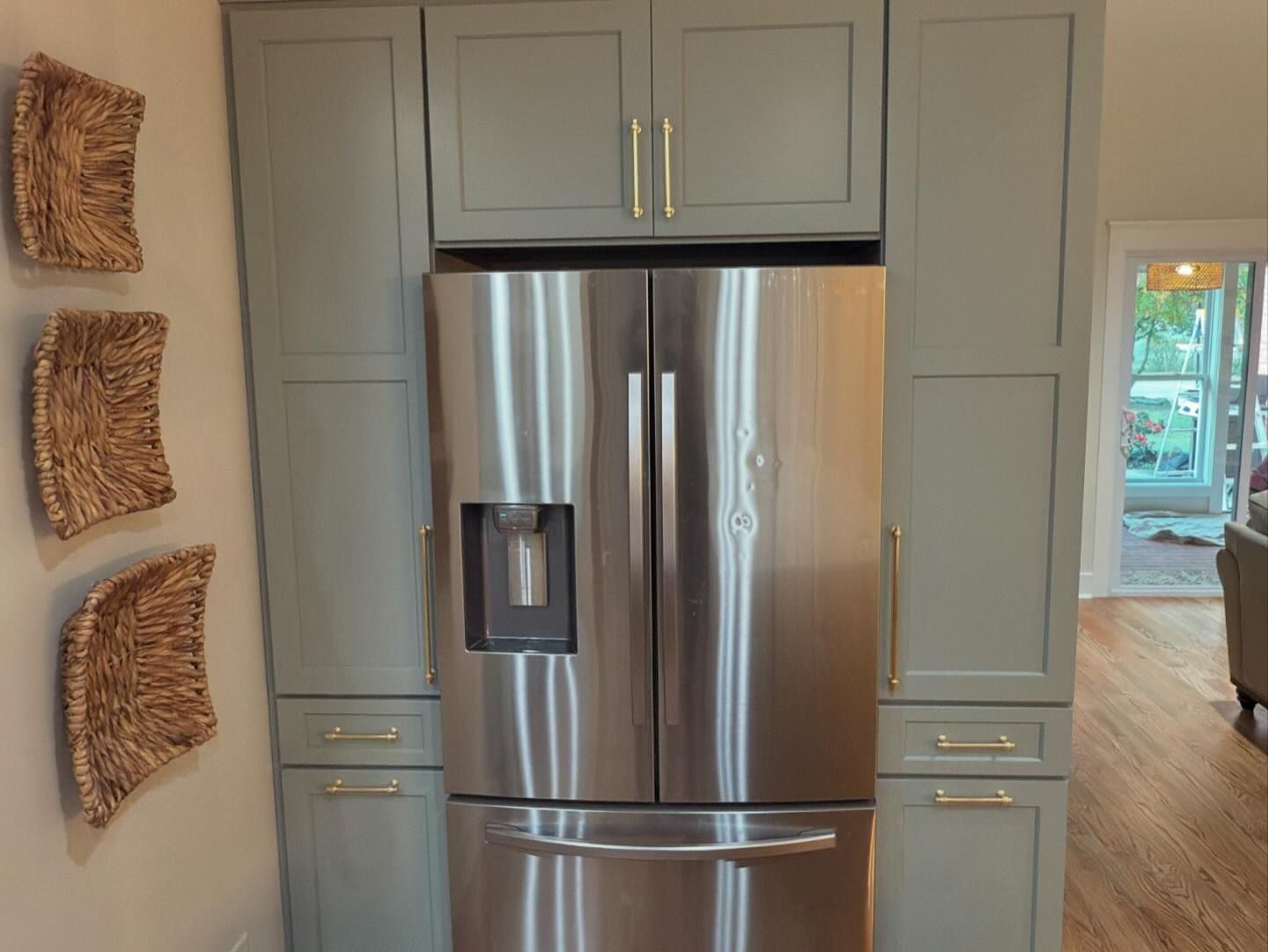 A stainless steel refrigerator in a kitchen with gray cabinets