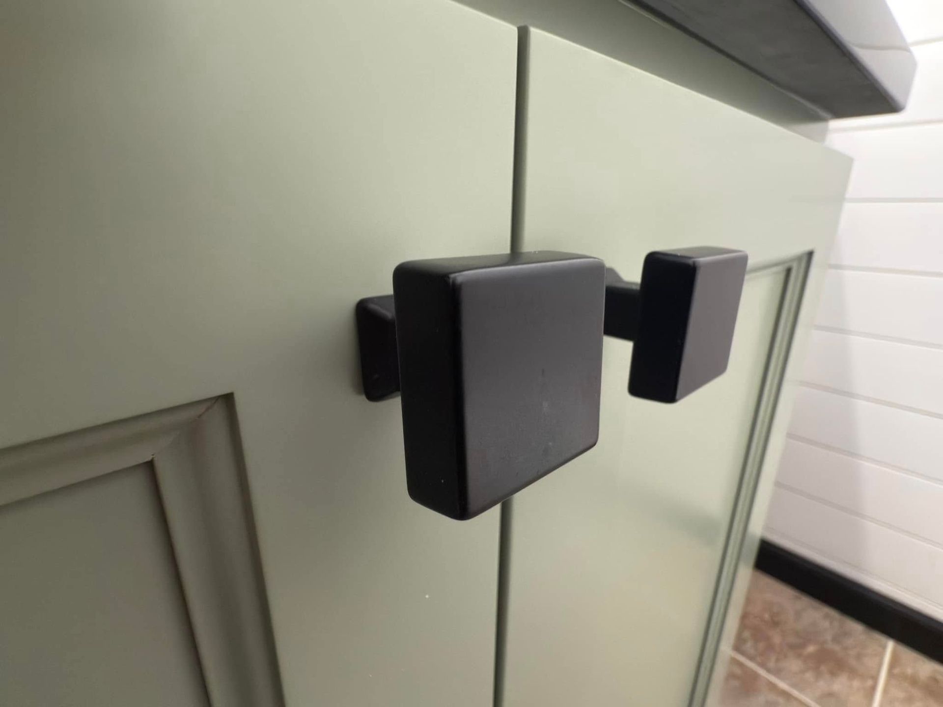 A close up of a black cabinet handle on a green cabinet