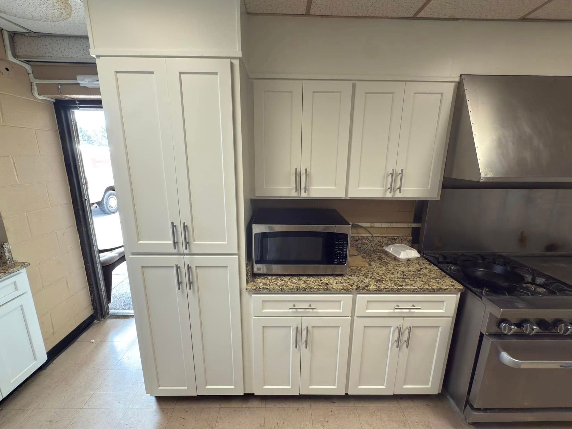White kitchen cabinets with a microwave, range, and outdoor door.