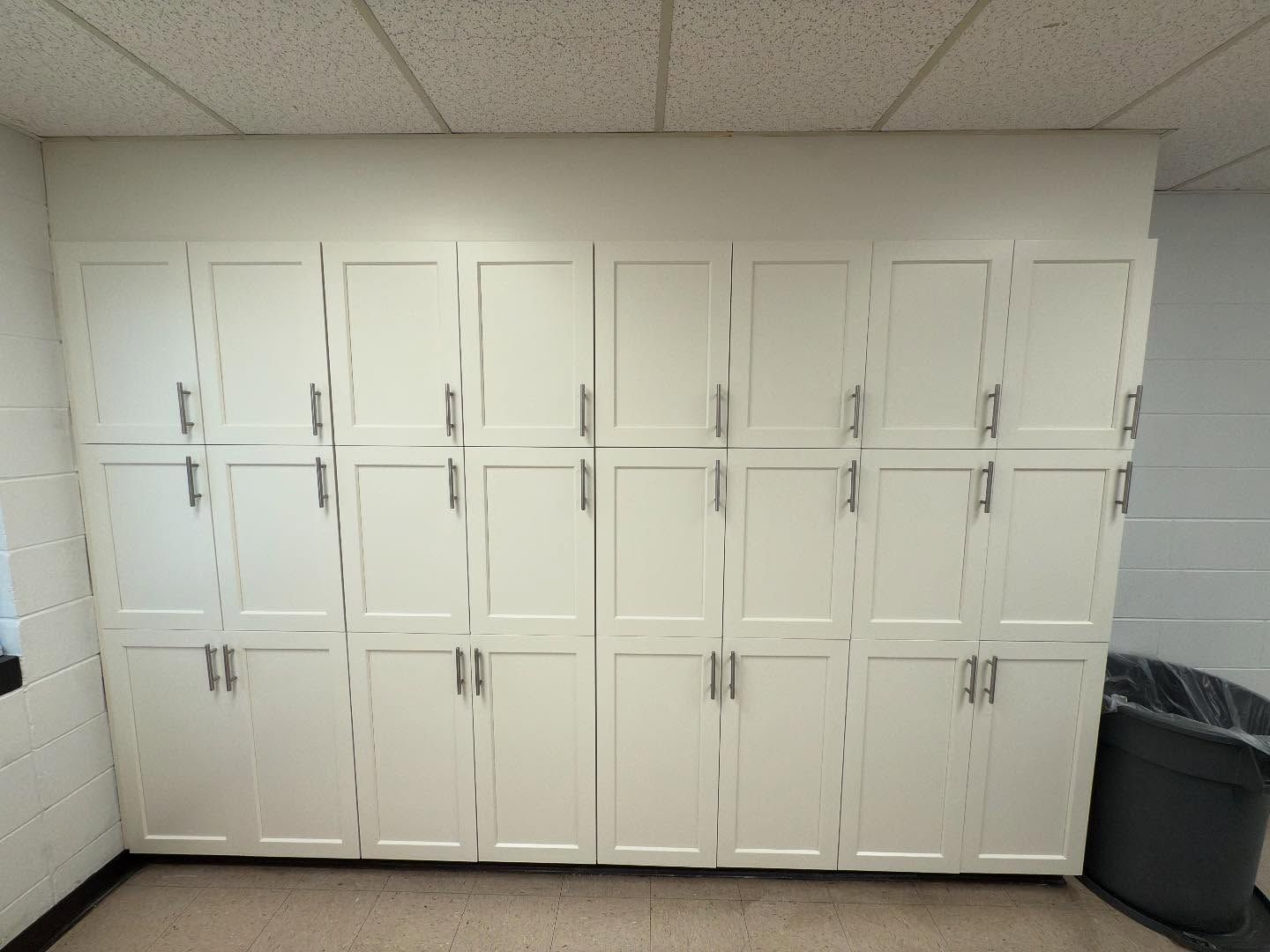 A room with a lot of white cabinets and a trash can.