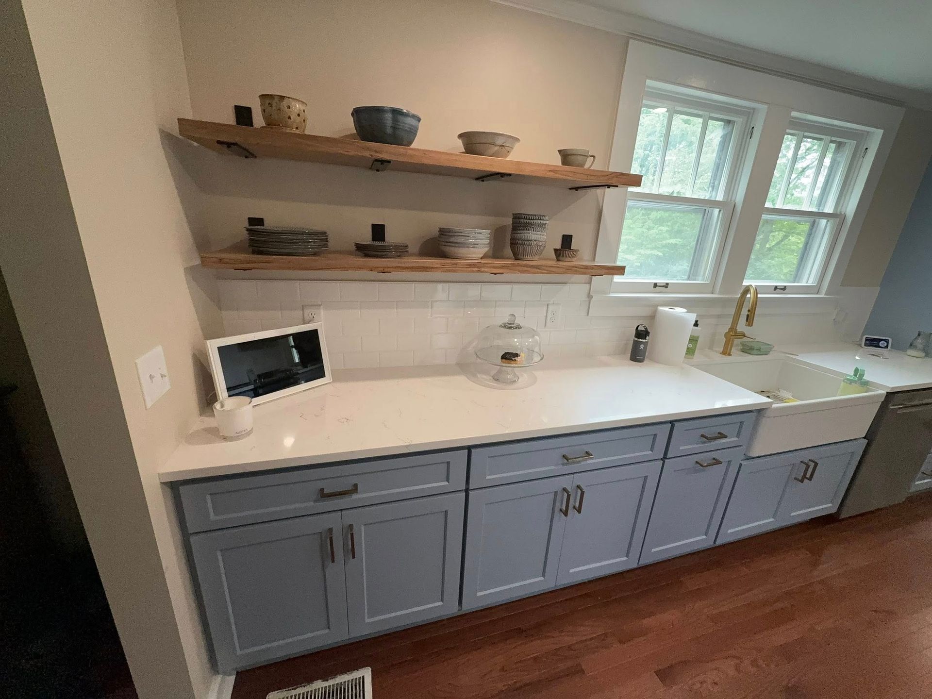 A kitchen with blue cabinets , white counter tops , and a sink.